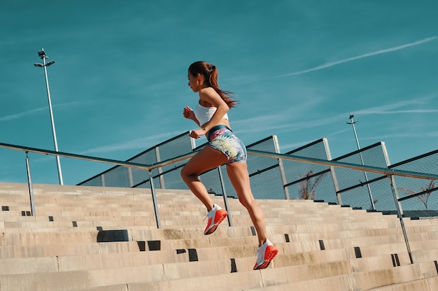 Se former pour devenir le meilleur. Toute la longueur de la belle jeune femme en vêtements de sport courant tout en faisant de l'exercice à l'extérieur