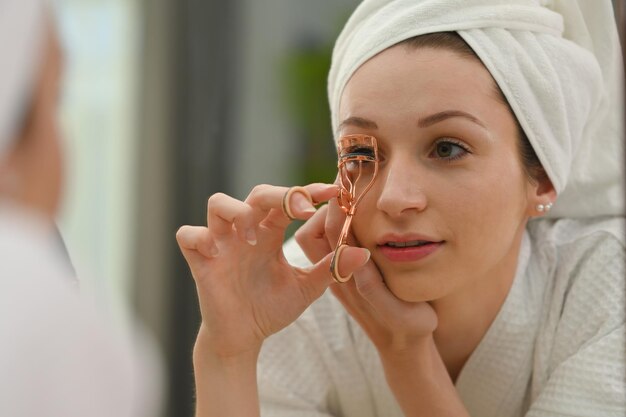 Se reflétant dans le miroir d'une belle femme caucasienne à l'aide d'un recourbe-cils curling cils Concept de soins de beauté et de cosmétiques