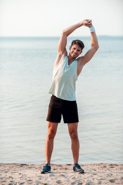 Se remettre en forme. Souriant jeune homme musclé s'entraînant en se tenant debout sur la berge