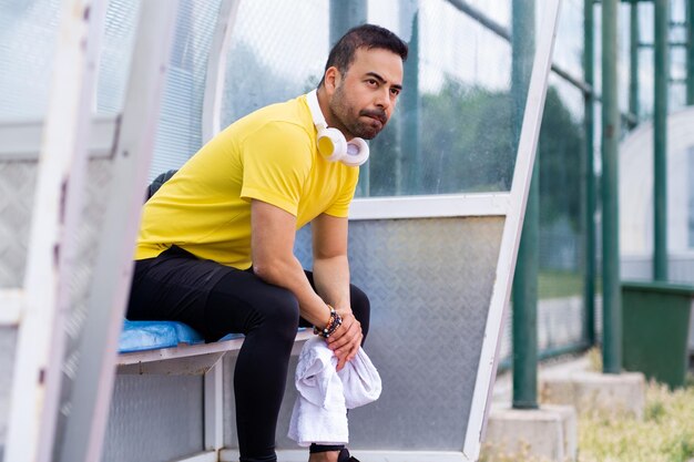 Se reposant dans la tonnelle du stade sportif de la ville, le sportif barbu portant des écouteurs