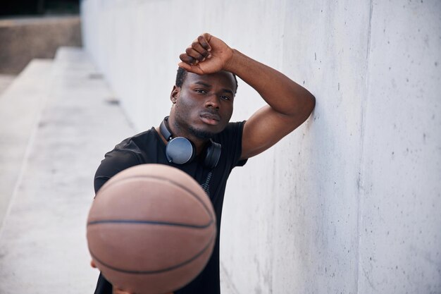 Photo se reposant sur le mur blanc, un jeune homme noir est avec une balle de basket-ball à l'extérieur.