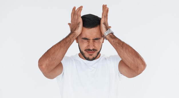 Se sent mal à la tête Jeune bel homme debout à l'intérieur sur fond blanc