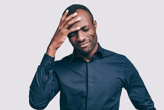 Se sentir bouleversé. Jeune homme africain frustré touchant la tête avec la main et gardant les yeux fermés en se tenant debout