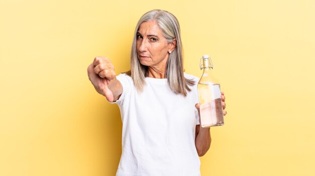 Se sentir en colère, agacé, déçu ou mécontent, montrant les pouces vers le bas avec un regard sérieux et tenant une bouteille d'eau