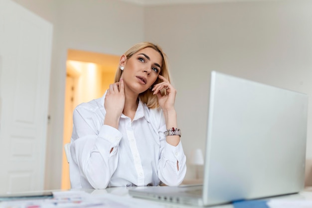 Se sentir épuisé Jeune femme frustrée à l'air épuisée assise sur son lieu de travail et portant ses lunettes à la main