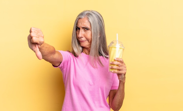 Se sentir fâché, en colère, ennuyé, déçu ou mécontent, montrant les pouces vers le bas avec un regard sérieux et tenant un milk-shake