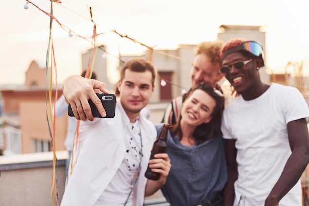 Se tenir ensemble et prendre un selfie Un groupe de jeunes en tenue décontractée fait la fête ensemble sur le toit pendant la journée