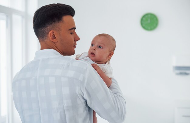 Se tient debout et tient bébé sur les mains. Le jeune pédiatre est à la clinique pendant la journée.