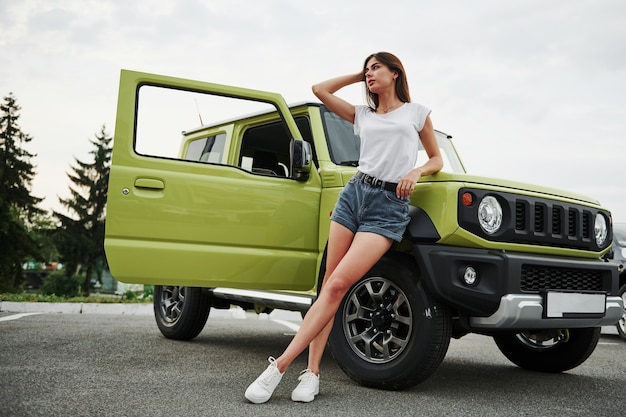 Se tient près du nouveau véhicule. Jolie femme dans la voiture moderne verte posant pour la caméra.