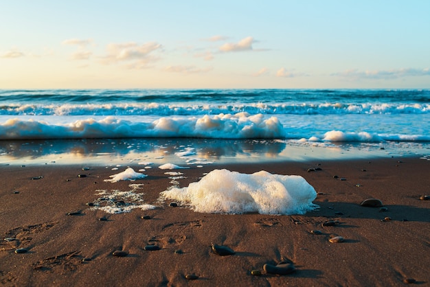 Seafoam sur le sable de la plage avec un paysage de ciel bleu clair