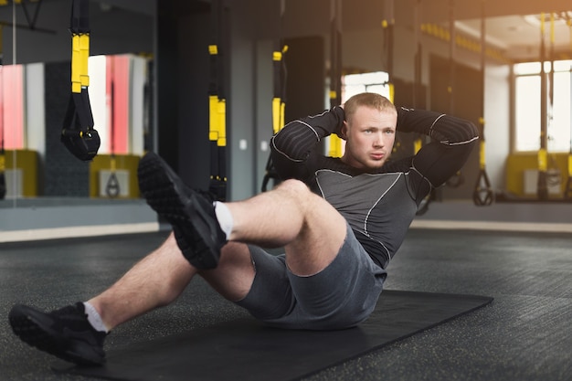 Séance d'entraînement de jeune homme dans un club de remise en forme. Portrait d'un homme de race blanche faisant de l'exercice, des redressements assis et des craquements pour les muscles abdominaux, s'entraînant à l'intérieur dans une salle de sport