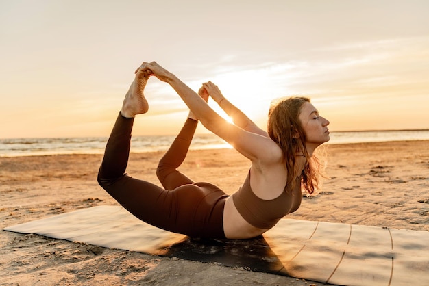 Séance d'entraînement de yoga au coucher du soleil une jeune femme mince beau corps asana exercice utilise un tapis sur le sable