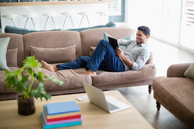 Séance homme, sur, sofa, et, utilisation, tablette numérique, dans, salle de séjour
