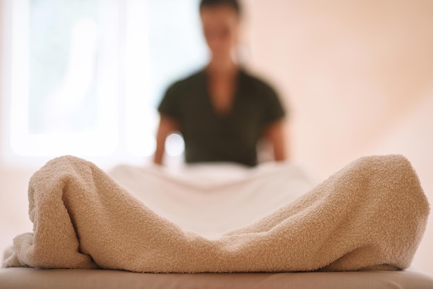 Séance de massage avec corps recouvert d'une serviette au premier plan et masseuse en arrière-plan flou