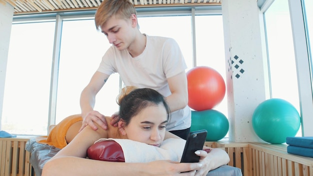 Séance de massage Jeune femme assise dans son téléphone tout en recevant un massage