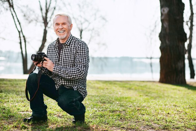 Séance photo. Cheerful senior man souriant et utilisant la caméra