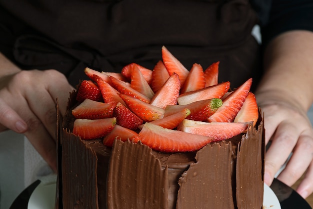 Séance photo avec décoration de gâteau au chocolat. Gâteau au chocolat recouvert de fraises, feuilles de basilic frais, confiture de mûres et assiettes de chocolat autour.