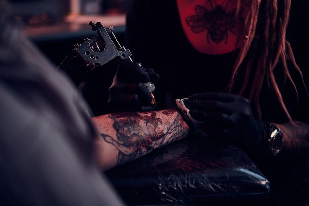 Séance photo en gros plan de la fabrication de tatouages, l'artiste travaille avec une machine à tatouer sur la main du client.