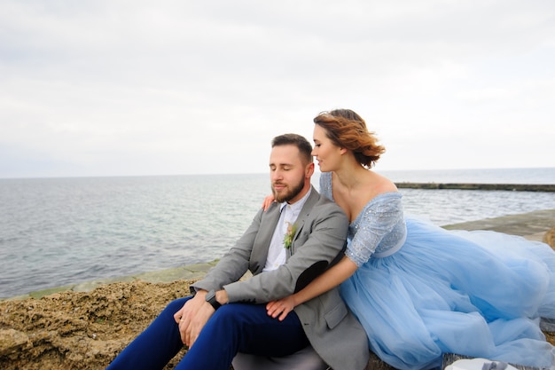 Séance photo de mariage d'un couple au bord de la mer. Robe de mariée bleue sur la mariée.