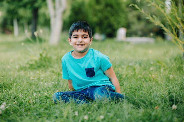 séance photo de style de vie d'un garçon drôle avec des vêtements bleus assis sur l'herbe dans un jardin verdoyant