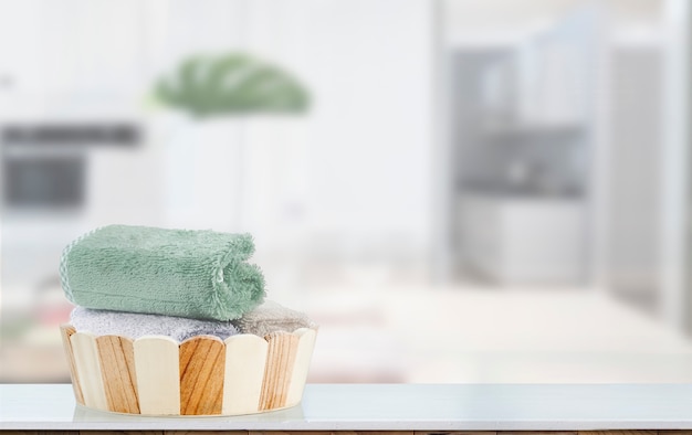 Seau de bain en bois maquette avec des serviettes sur une table blanche avec fond de salle blanche estompée.