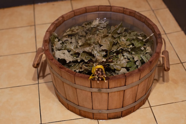 Seau en bois rempli d'eau avec un balai fait à la main trempant dans un sauna lumineux Avoir un temps de repos sain dans un bain avec des amis pendant le week-end