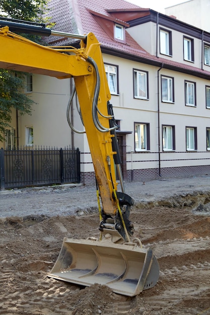 Le seau d'une excavatrice engagée dans la réparation et la pose d'une route sur le fond des maisons d'une rue de la ville