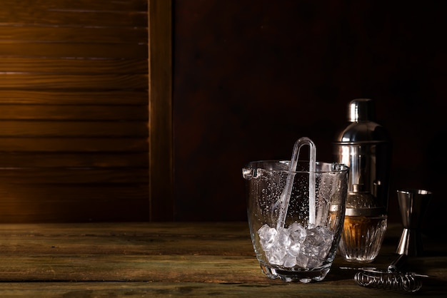 Seau à glace en verre avec accessoires de bar sur fond en bois foncé