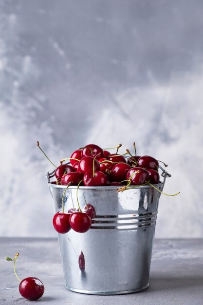 Seau en métal avec cerise douce rouge sur fond gris.