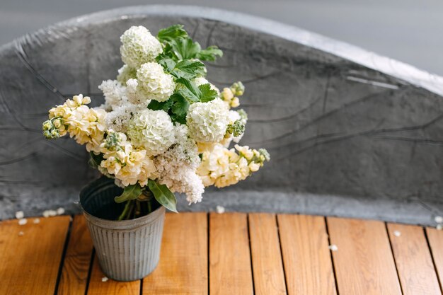 Seau métallique avec des fleurs de lilas et de matthiola blanc sur un banc en bois