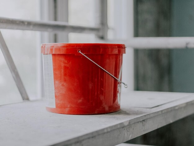 Un seau rouge avec du mastic et un couvercle bien fermé se trouve sur un échafaudage métallique sale