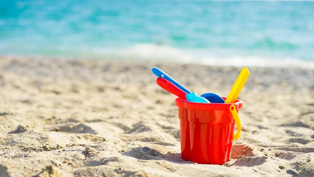 Seau rouge pour enfants avec du sable et des jouets au bord de la mer