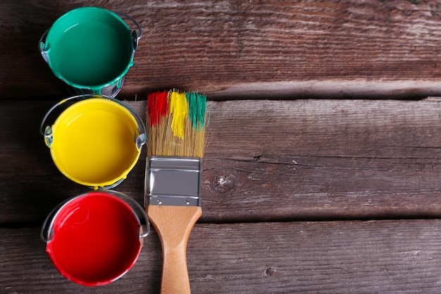 Photo seaux en métal avec de la peinture colorée près de la brosse sur fond de bois