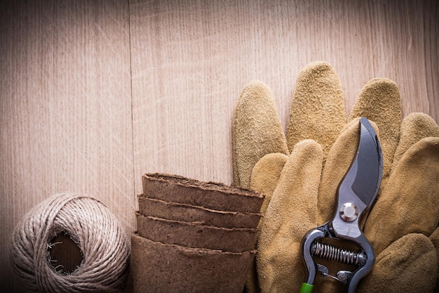 Sécateur pointu gants de sécurité en cuir pots de tourbe et écheveau de ficelle sur planche de bois vintage concept de jardinage