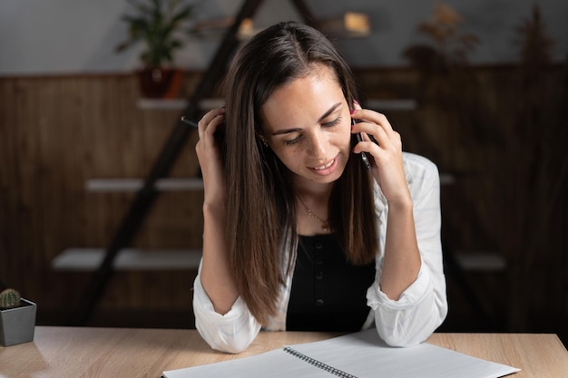 Une secrétaire de bureau sérieuse écoute une conversation téléphonique sur son smartphone alors qu'elle est assise à son bureau La fille parle sur un téléphone portable discutant des plans avec le directeur