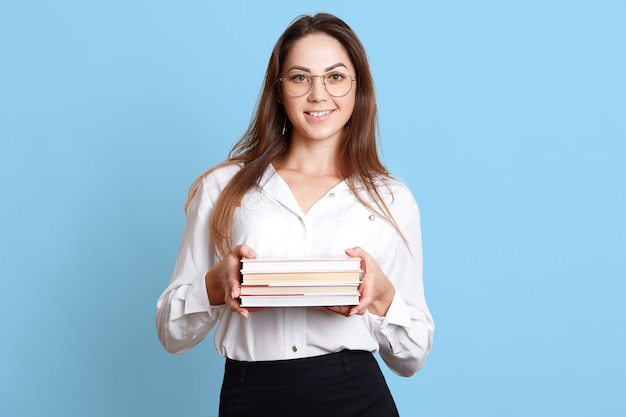 Secrétaire énergétique mince et souriante tenant une pile de livres dans les deux mains