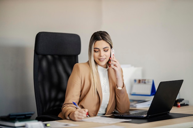 Une secrétaire est assise au bureau et prend rendez-vous tout en parlant au téléphone avec le client