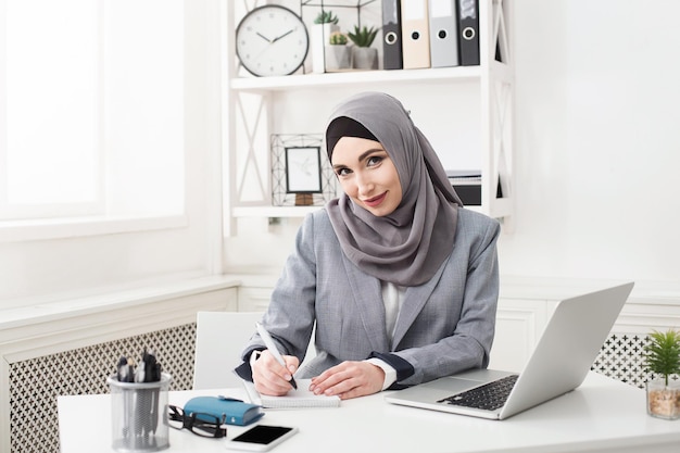 Secrétaire de femme islamique prenant des notes sur le lieu de travail au bureau