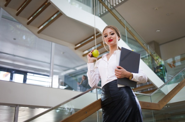 Une secrétaire avec des papiers et une pomme dans les mains va déjeuner dans les escaliers du bureau. Concept de femme d'affaires