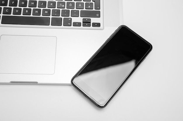 Section basse du clavier d'un ordinateur portable haut de gamme et d'un smartphone moderne sur un fond blanc