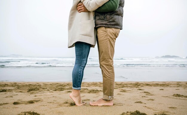 Section basse du couple debout pieds nus sur la plage