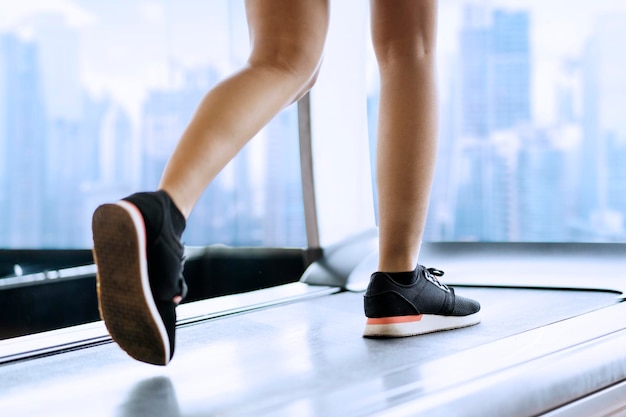 Section basse d'une femme courant sur un tapis roulant au gymnase