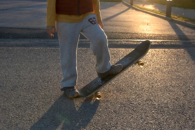 Section basse d'un garçon faisant du skateboard sur la route au coucher du soleil