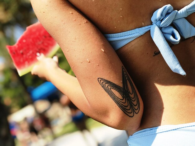 Section du milieu d'une adolescente en bikini avec un tatouage sur la main