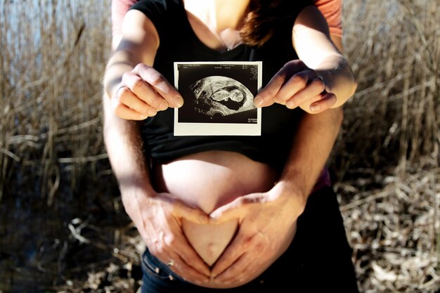 Photo section médiane d'un couple enceinte donnant une forme de cœur tout en tenant un transfert d'impression d'image sur terre