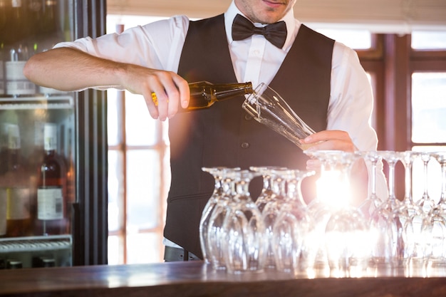 Photo section médiane du barman versant une bière dans un verre