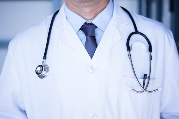 Section médiane du médecin de sexe masculin en blouse de laboratoire portant un stéthoscope autour du cou à l'hôpital
