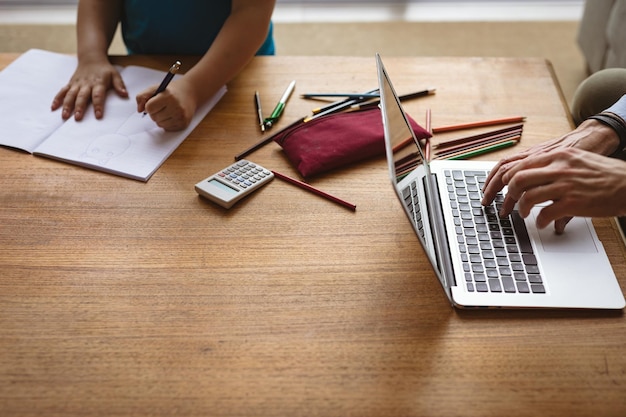 Section médiane du père utilisant un ordinateur portable pendant que son fils fait ses devoirs à la maison