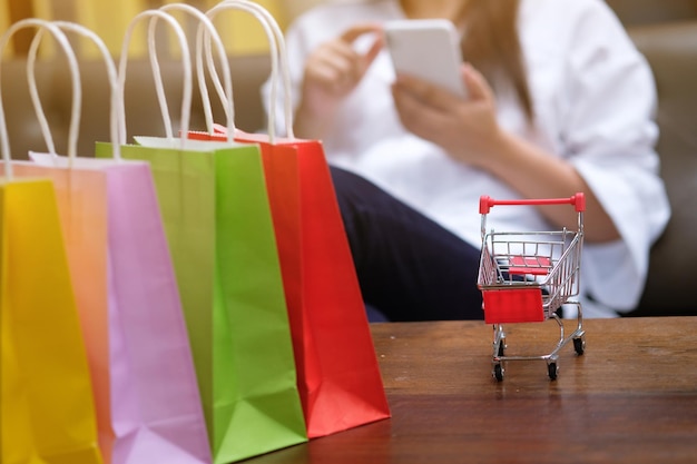 Section médiane d'une femme avec un chariot d'achat et des sacs sur une table en bois à l'aide d'un téléphone portable