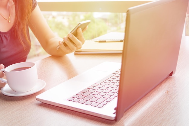 Section médiane d'une femme avec du café en utilisant le téléphone par ordinateur portable et du café sur la table